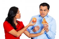 Женщина предлагает мужчине яблоко вместо пиццы, которую тот держит в руках. Весь облик мужчины выражает отвращение.