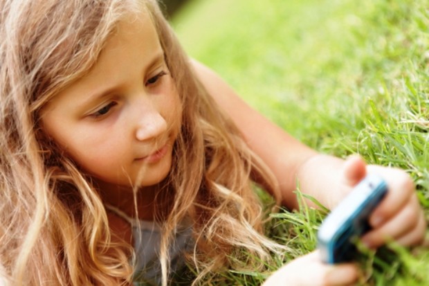 Длинноволоса девочка с мобильным телефоном в руках лежит на траве
