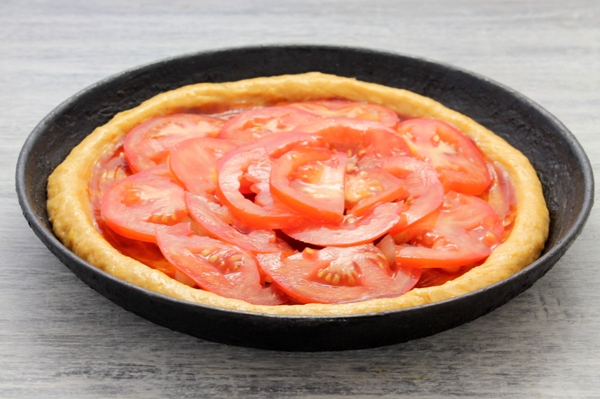 На тесто для пиццы выкладываются нарезанные помидоры 