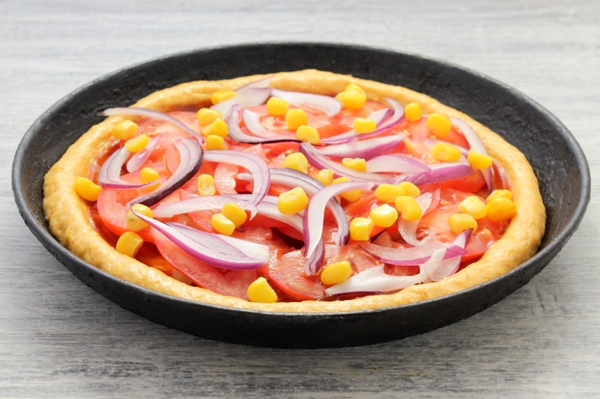 Поверх помидоров на сырую пиццы раскладывается репчатый лук и кукуруза