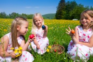 Три девочки на лугу играют пасхальными яйцами