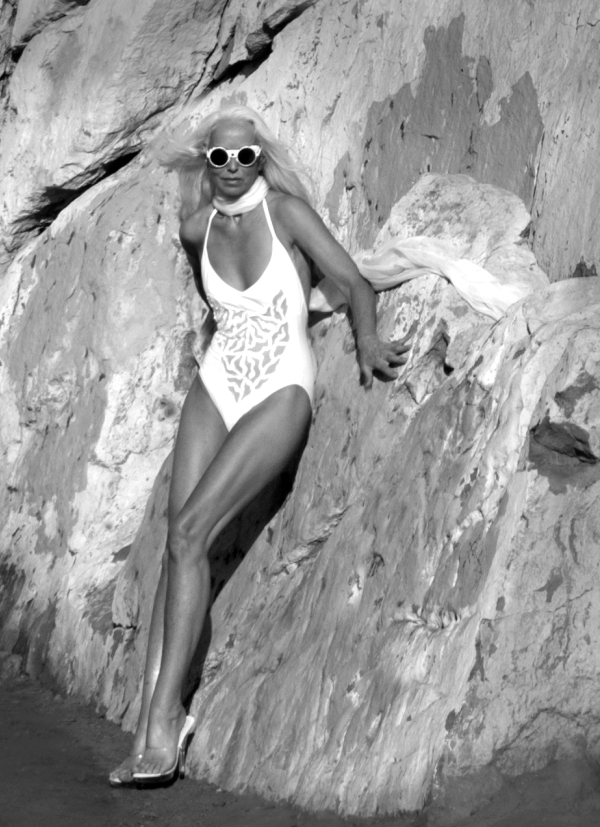 Ясмина Росси в белом купальнике, с белым шарфом на фоне скалы